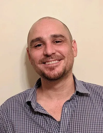 Jesse Jonesberg, smiling, against a warm wall